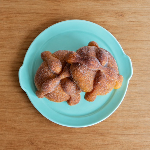 Two pan de muerto pastries on a turquoise plate, overhead view