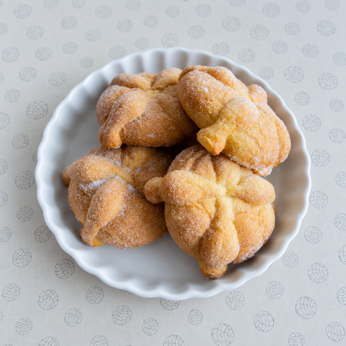 Four sugar-coated vegan pan de muerto pastries on a white plate