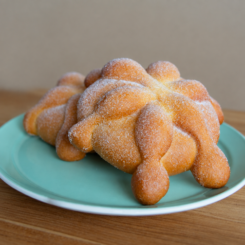 Close-up of two sugar-coated pan de muerto pastries on a turquoise plate