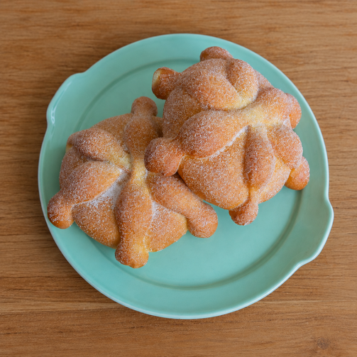 Two sugar-coated pan de muerto pastries on a turquoise plate